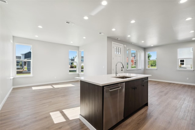 kitchen with sink, a kitchen island with sink, stainless steel dishwasher, dark brown cabinetry, and light hardwood / wood-style flooring