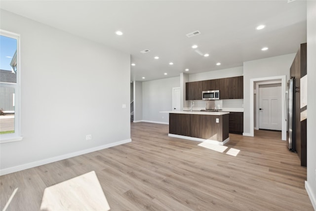 kitchen featuring a healthy amount of sunlight, appliances with stainless steel finishes, a center island with sink, and light wood-type flooring