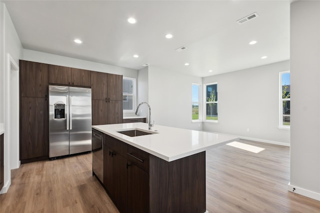 kitchen with stainless steel appliances, sink, a center island with sink, and light wood-type flooring