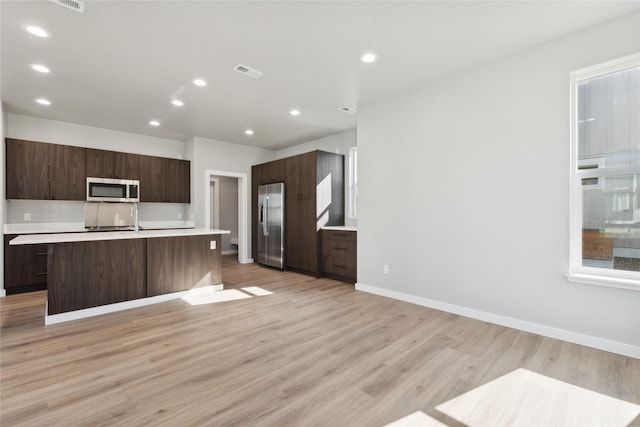 kitchen featuring an island with sink, appliances with stainless steel finishes, dark brown cabinets, and light hardwood / wood-style floors