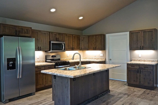 kitchen featuring lofted ceiling, appliances with stainless steel finishes, a kitchen island with sink, light countertops, and a sink