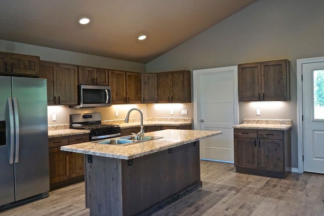 kitchen with lofted ceiling, appliances with stainless steel finishes, a kitchen island with sink, light countertops, and a sink