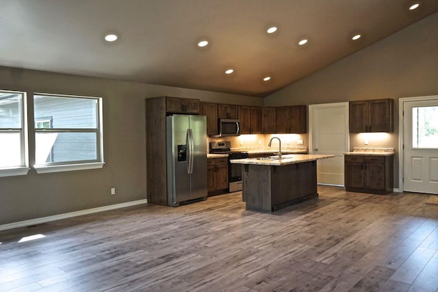 kitchen featuring light stone counters, wood finished floors, a sink, appliances with stainless steel finishes, and a center island with sink