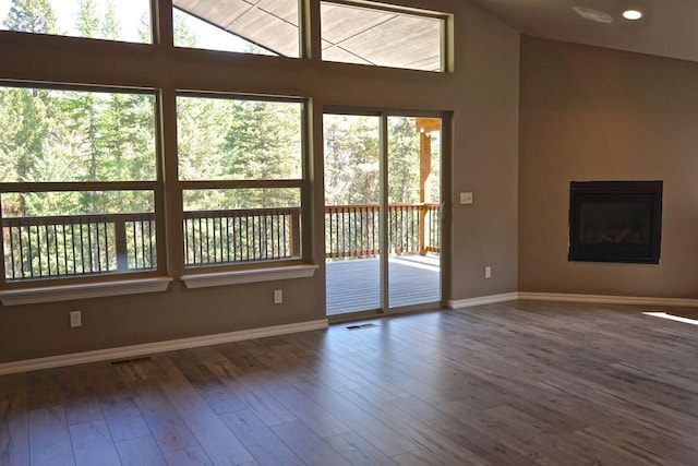 unfurnished living room with baseboards, visible vents, wood finished floors, and a glass covered fireplace