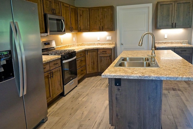 kitchen featuring light wood finished floors, an island with sink, appliances with stainless steel finishes, light countertops, and a sink