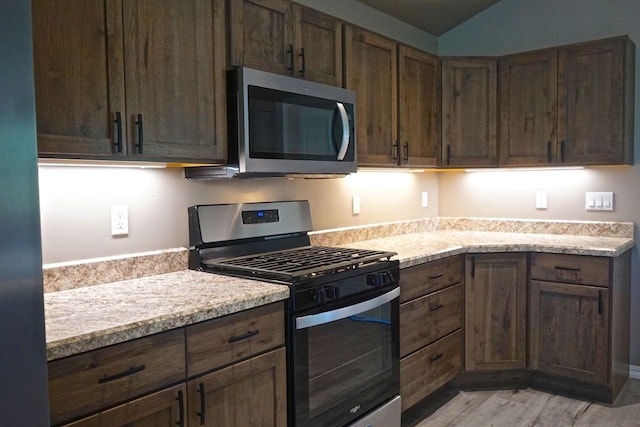 kitchen with stainless steel appliances, lofted ceiling, light wood finished floors, and light stone counters