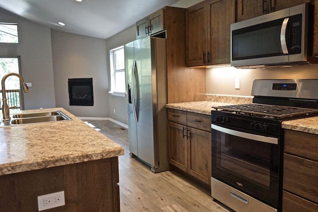 kitchen featuring a glass covered fireplace, light wood-style flooring, appliances with stainless steel finishes, light countertops, and a sink