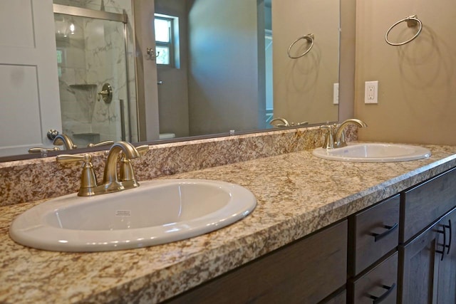 full bathroom with toilet, double vanity, a sink, and a marble finish shower