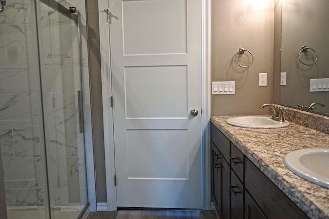 full bath with a sink, a marble finish shower, and double vanity