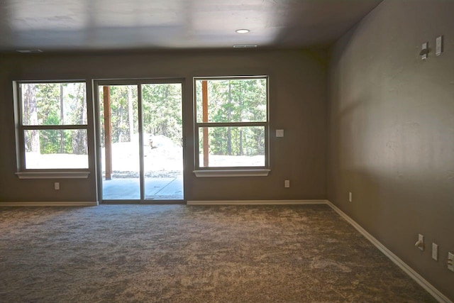 unfurnished room with baseboards, dark colored carpet, visible vents, and a healthy amount of sunlight