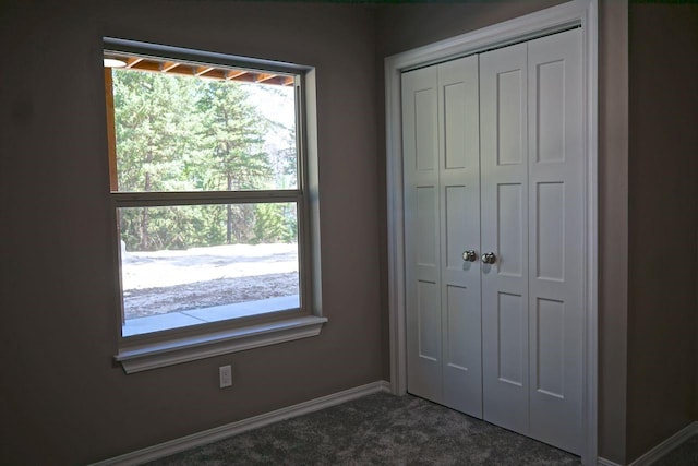 unfurnished bedroom with a closet, dark carpet, and baseboards