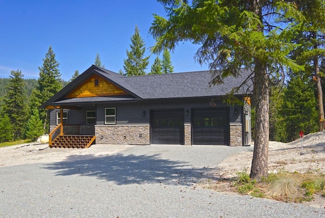 view of front of house featuring gravel driveway, stone siding, an attached garage, and covered porch