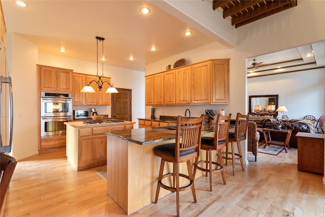 kitchen featuring appliances with stainless steel finishes, pendant lighting, beam ceiling, light hardwood / wood-style flooring, and a center island