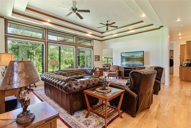 living room featuring a raised ceiling, ceiling fan, a towering ceiling, ornamental molding, and light hardwood / wood-style floors