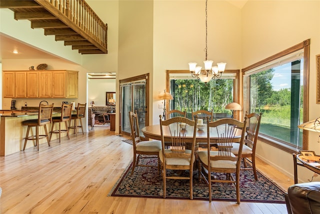 dining area featuring an inviting chandelier, a towering ceiling, beamed ceiling, and light wood-type flooring