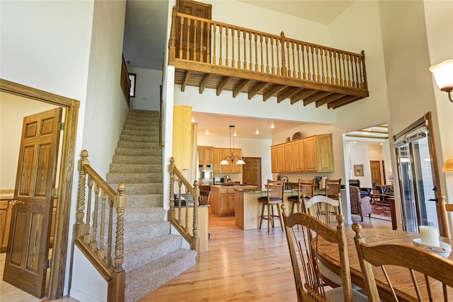 dining room with beam ceiling, a towering ceiling, and light hardwood / wood-style floors