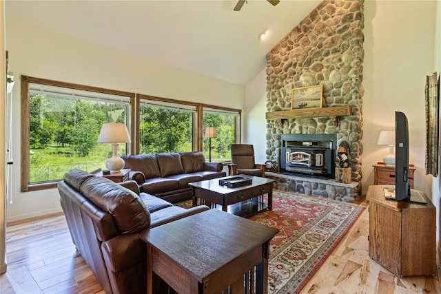 living room with high vaulted ceiling, a wood stove, a wealth of natural light, and light hardwood / wood-style flooring