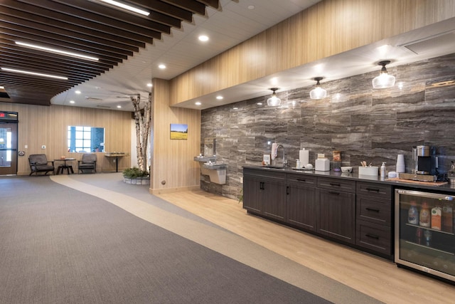 bar featuring dark brown cabinets, light wood-type flooring, sink, beverage cooler, and wood walls