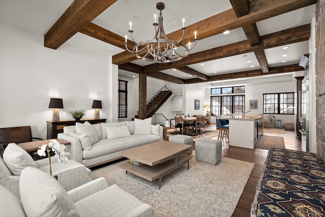 living room with beam ceiling, dark wood-type flooring, a chandelier, and a stone fireplace