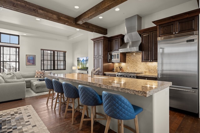 kitchen with built in appliances, a kitchen island with sink, wall chimney exhaust hood, and sink