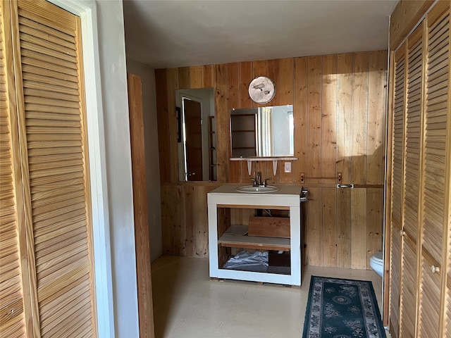 bathroom with concrete flooring, vanity, toilet, and wood walls