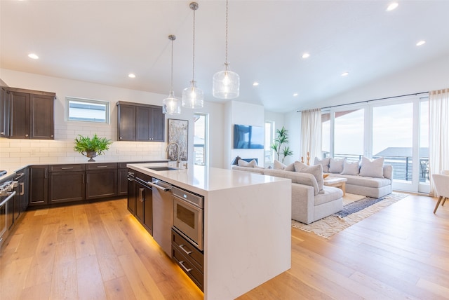 kitchen with hanging light fixtures, tasteful backsplash, an island with sink, dishwasher, and light hardwood / wood-style flooring