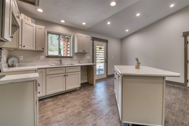 kitchen with light stone countertops, a kitchen island, white cabinets, sink, and light wood-type flooring