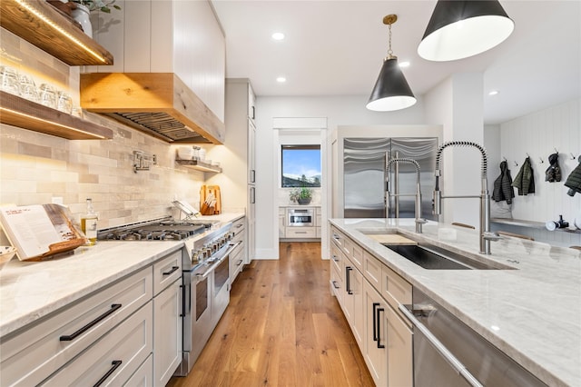 kitchen featuring light stone counters, sink, premium appliances, and decorative light fixtures