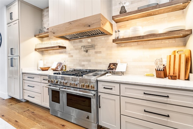 kitchen featuring tasteful backsplash, light hardwood / wood-style floors, range with two ovens, custom range hood, and light stone counters