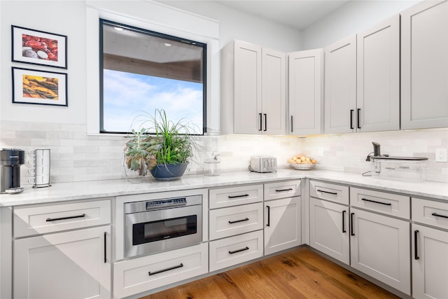 kitchen featuring light stone counters, decorative backsplash, white cabinets, and light wood-type flooring