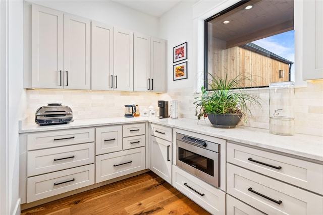 kitchen featuring light hardwood / wood-style floors, stainless steel microwave, decorative backsplash, light stone countertops, and white cabinets