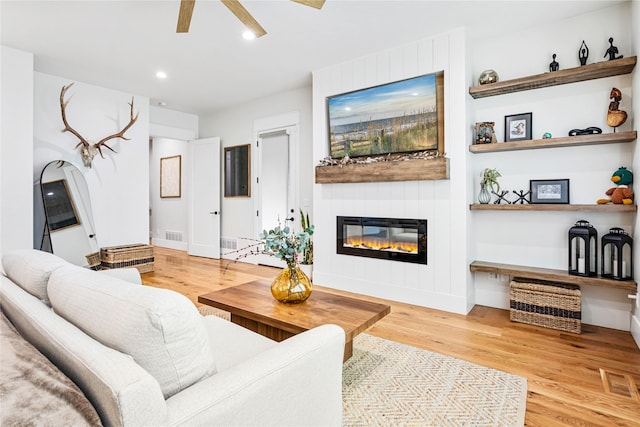 living room featuring ceiling fan, a large fireplace, and light wood-type flooring