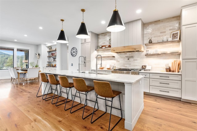 kitchen with white cabinetry, an island with sink, backsplash, decorative light fixtures, and light hardwood / wood-style flooring