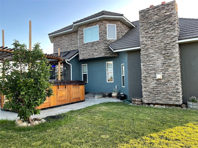 back of property with a yard, a pergola, and a hot tub