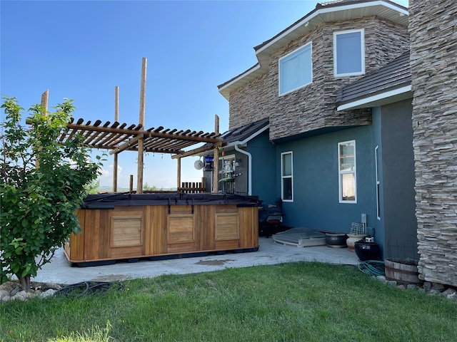 back of house with a hot tub, a pergola, and a yard