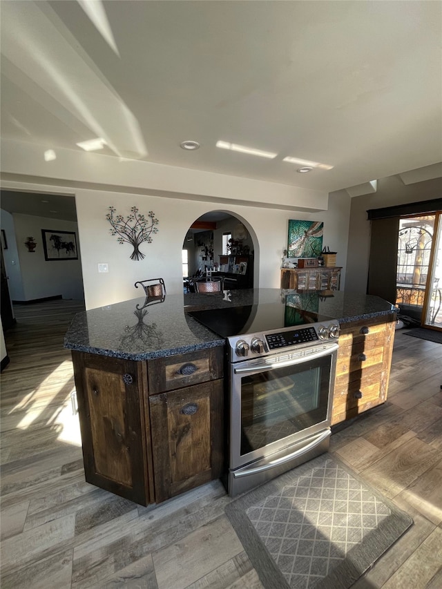 kitchen featuring hardwood / wood-style floors, dark stone countertops, dark brown cabinetry, stainless steel electric range, and a kitchen island