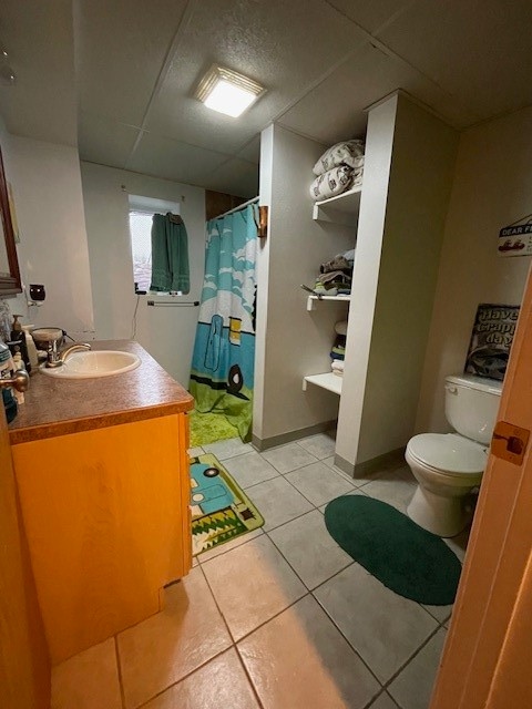 bathroom with tile flooring, vanity, toilet, and a drop ceiling