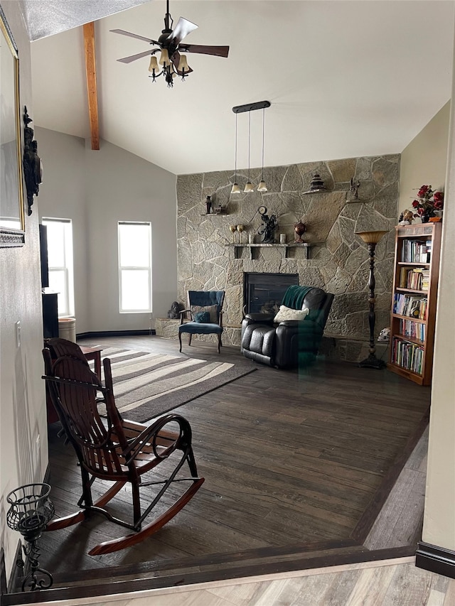 living room featuring vaulted ceiling with beams, hardwood / wood-style floors, a stone fireplace, and ceiling fan