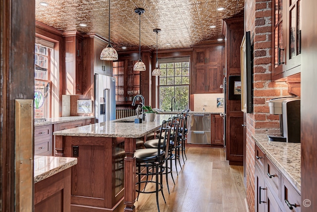 kitchen featuring high end refrigerator, light hardwood / wood-style floors, a breakfast bar area, decorative light fixtures, and a kitchen island with sink