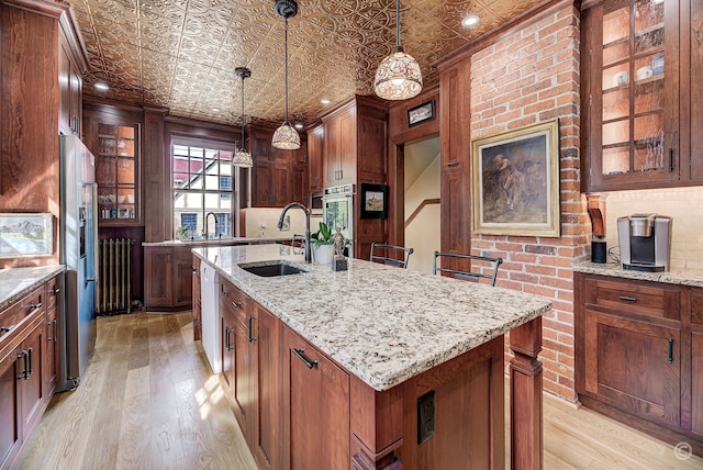 kitchen with sink, a center island with sink, light wood-type flooring, and pendant lighting