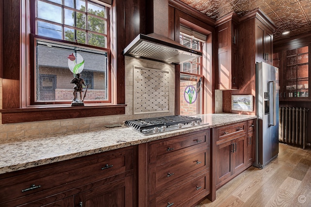 interior space featuring appliances with stainless steel finishes, backsplash, light wood-type flooring, premium range hood, and light stone countertops