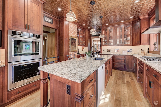 kitchen featuring a kitchen island with sink, sink, stainless steel appliances, light hardwood / wood-style flooring, and pendant lighting