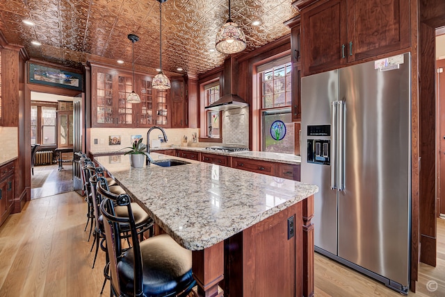 kitchen featuring a center island, wall chimney exhaust hood, sink, stainless steel appliances, and light hardwood / wood-style flooring