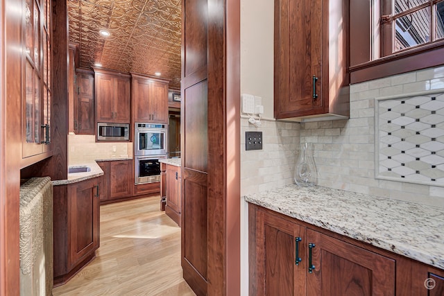 kitchen with tasteful backsplash, light hardwood / wood-style floors, stainless steel appliances, and light stone counters