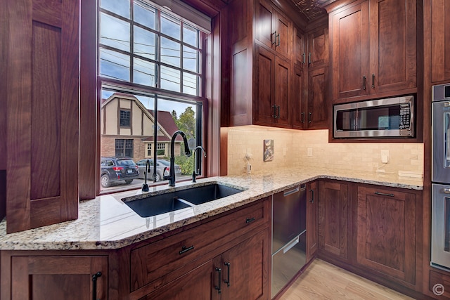 kitchen featuring appliances with stainless steel finishes, backsplash, light stone counters, sink, and light wood-type flooring