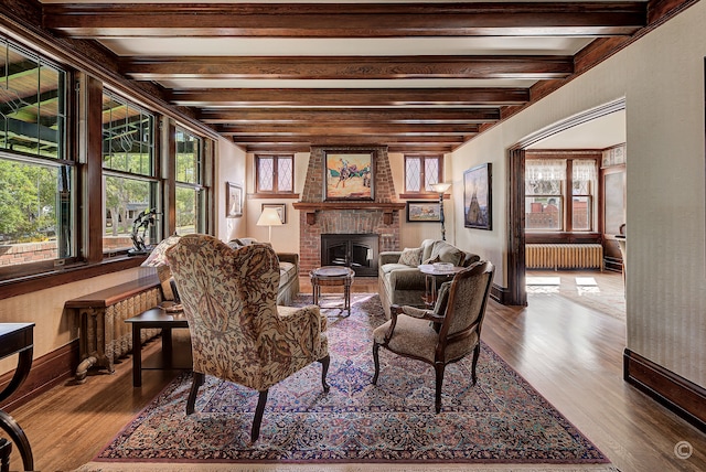 living room featuring radiator, wood-type flooring, beamed ceiling, and a fireplace