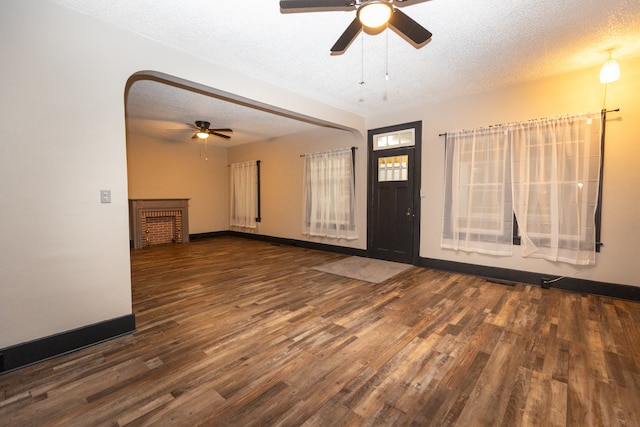 unfurnished living room with dark wood-type flooring, ceiling fan, a brick fireplace, and a textured ceiling