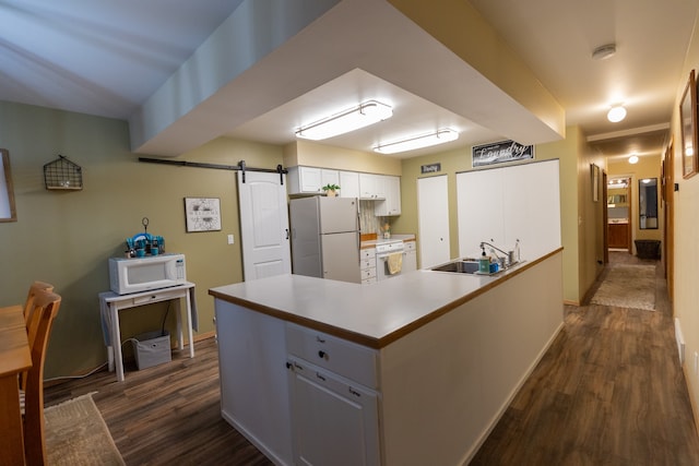 kitchen with white appliances, dark wood-type flooring, sink, a barn door, and white cabinets