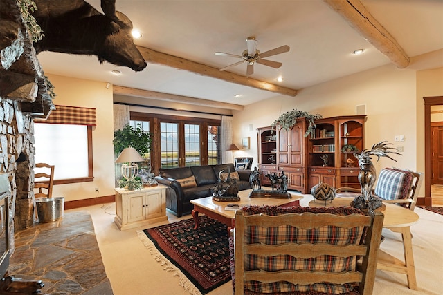 living room featuring light colored carpet, ceiling fan, french doors, beamed ceiling, and a stone fireplace