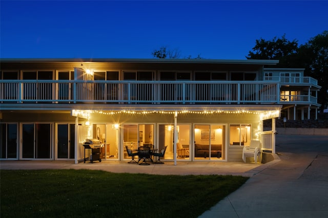 back house at twilight with a balcony, a yard, and a patio